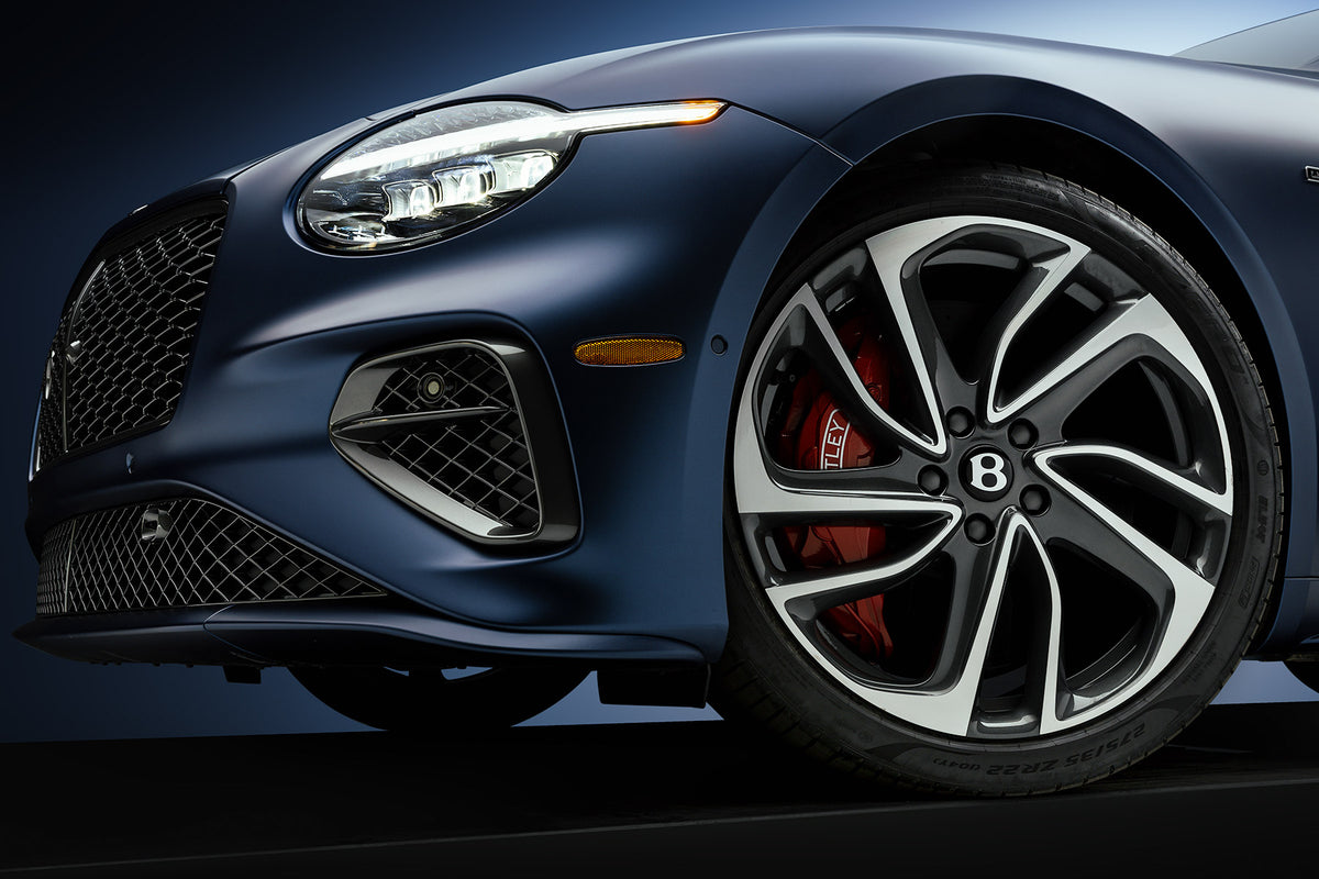 Close detail of a satin blue Bentley Continental GT front wheel, red caliper, and headlight in studio light, by Niaz Uddin