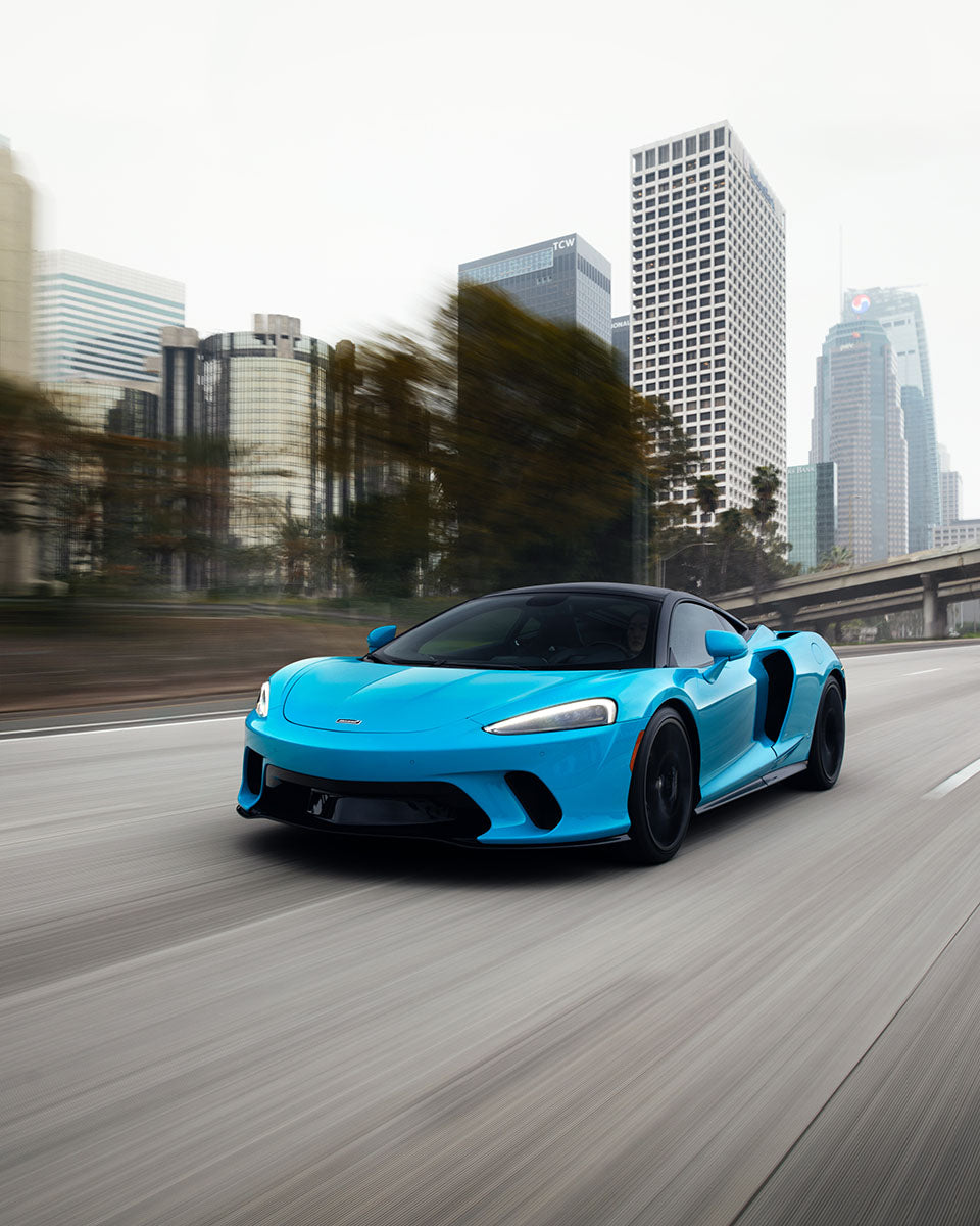 Cyan McLaren GT driving in motion past downtown Los Angeles high-rises, by Niaz Uddin