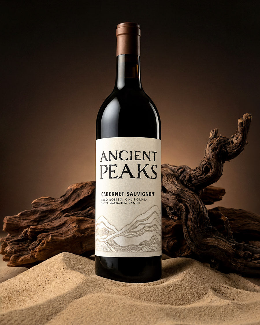 Ancient Peaks Cabernet Sauvignon bottle standing in sand with driftwood, Santa Margarita Ranch, Paso Robles, wine photography by Niaz Uddin