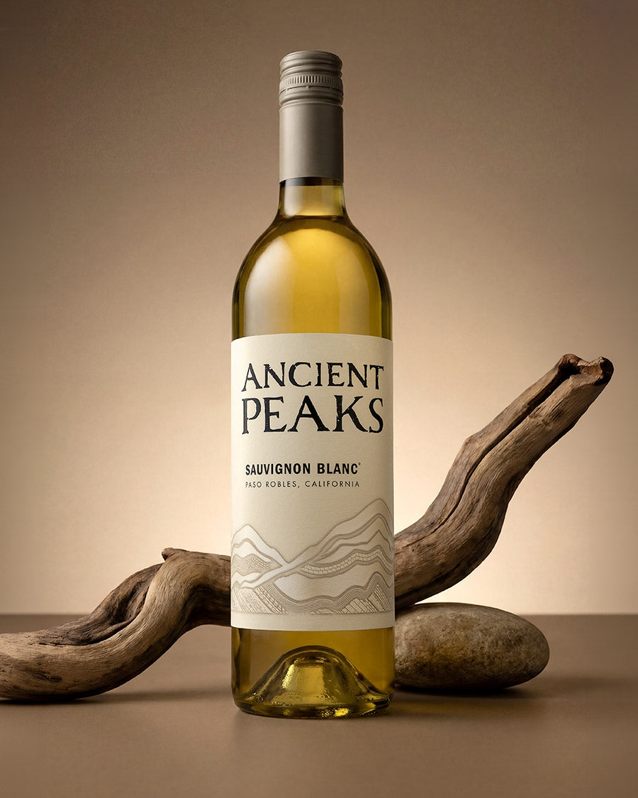 Ancient Peaks Sauvignon Blanc bottle with driftwood and stone on a warm beige backdrop, Paso Robles wine photography by Niaz Uddin