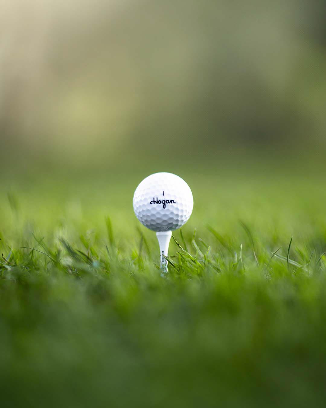 Ben Hogan golf ball on a white tee in the grass, low-angle close-up, by Niaz Uddin