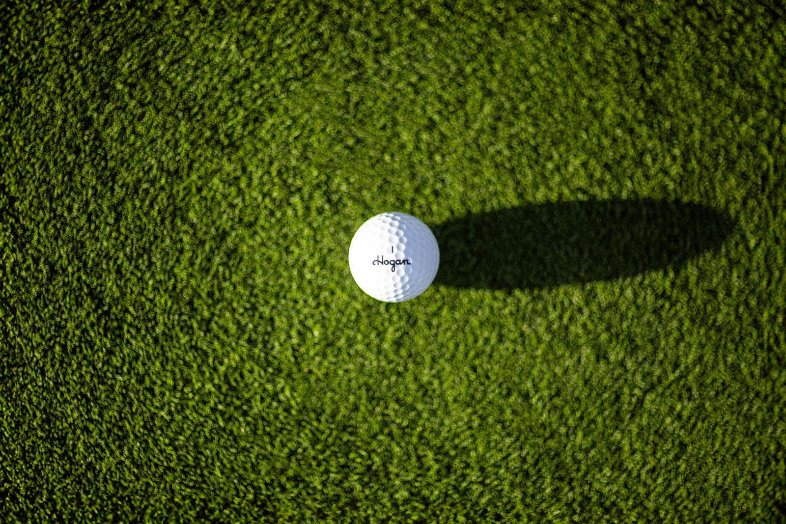 Top-down view of a Ben Hogan golf ball on the green with a long shadow, by Niaz Uddin