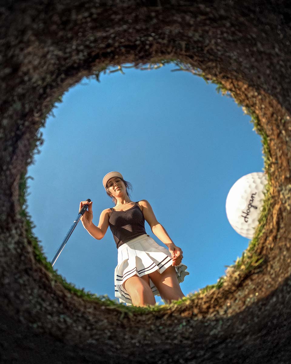 Looking up from inside the cup at a golfer and a Ben Hogan golf ball about to drop, by Niaz Uddin