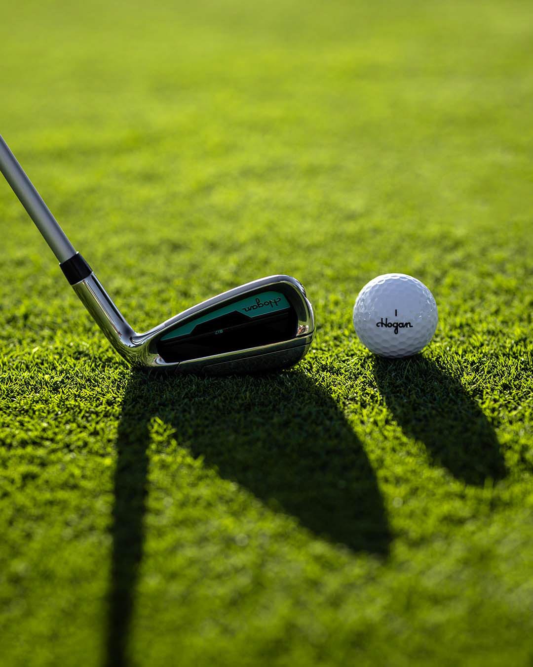 Chrome Ben Hogan iron beside a golf ball on sunlit grass casting a long shadow, by Niaz Uddin