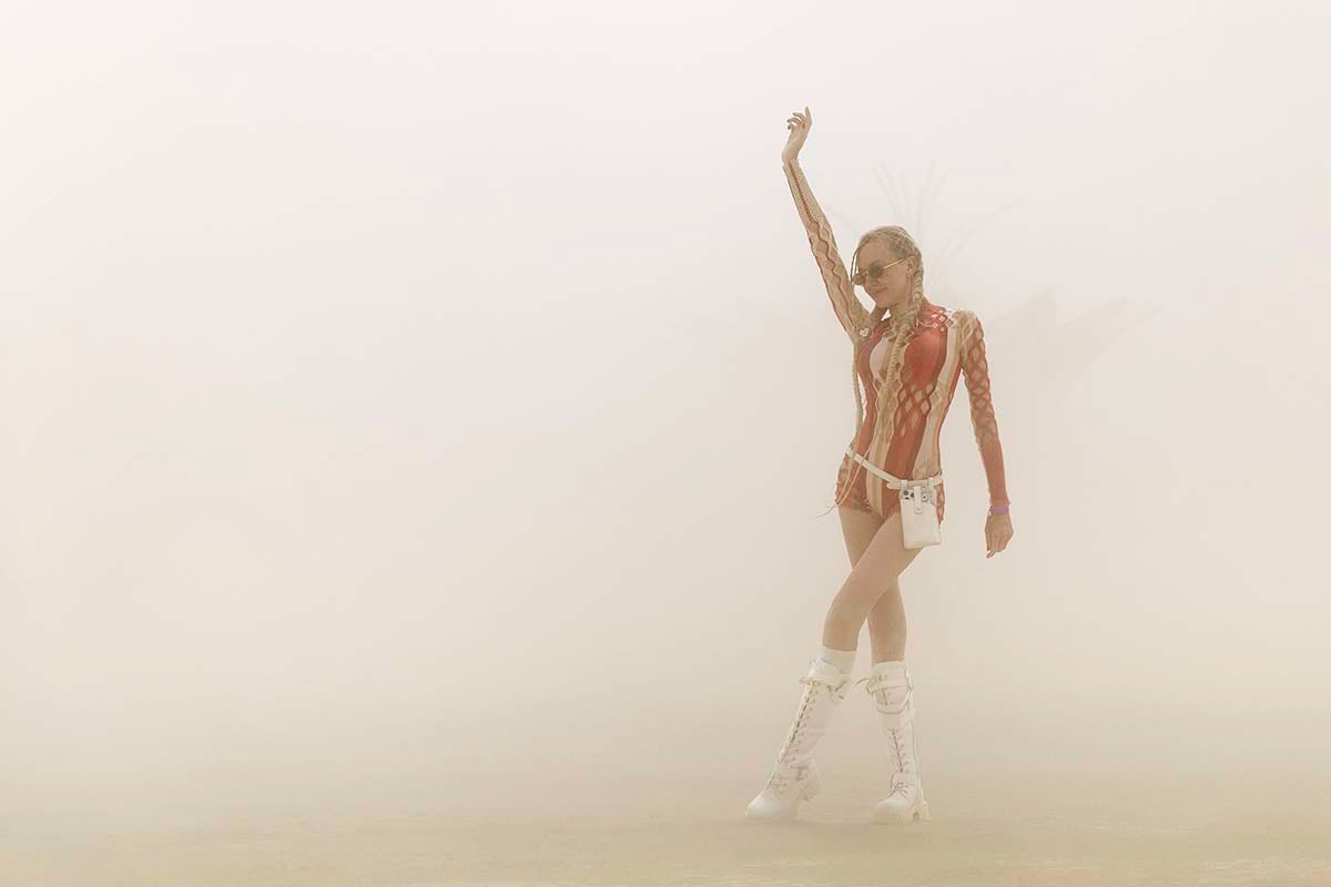 Woman in a red and white bodysuit dancing in a whiteout dust storm on the playa, Burning Man 2026, by Niaz Uddin