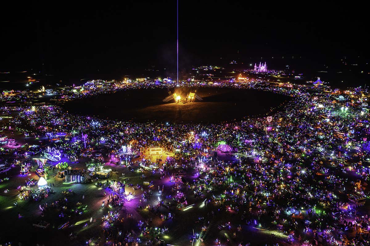 Aerial view of the Man burn at night, ringed by thousands of people and glowing art cars, Burning Man 2026, by Niaz Uddin