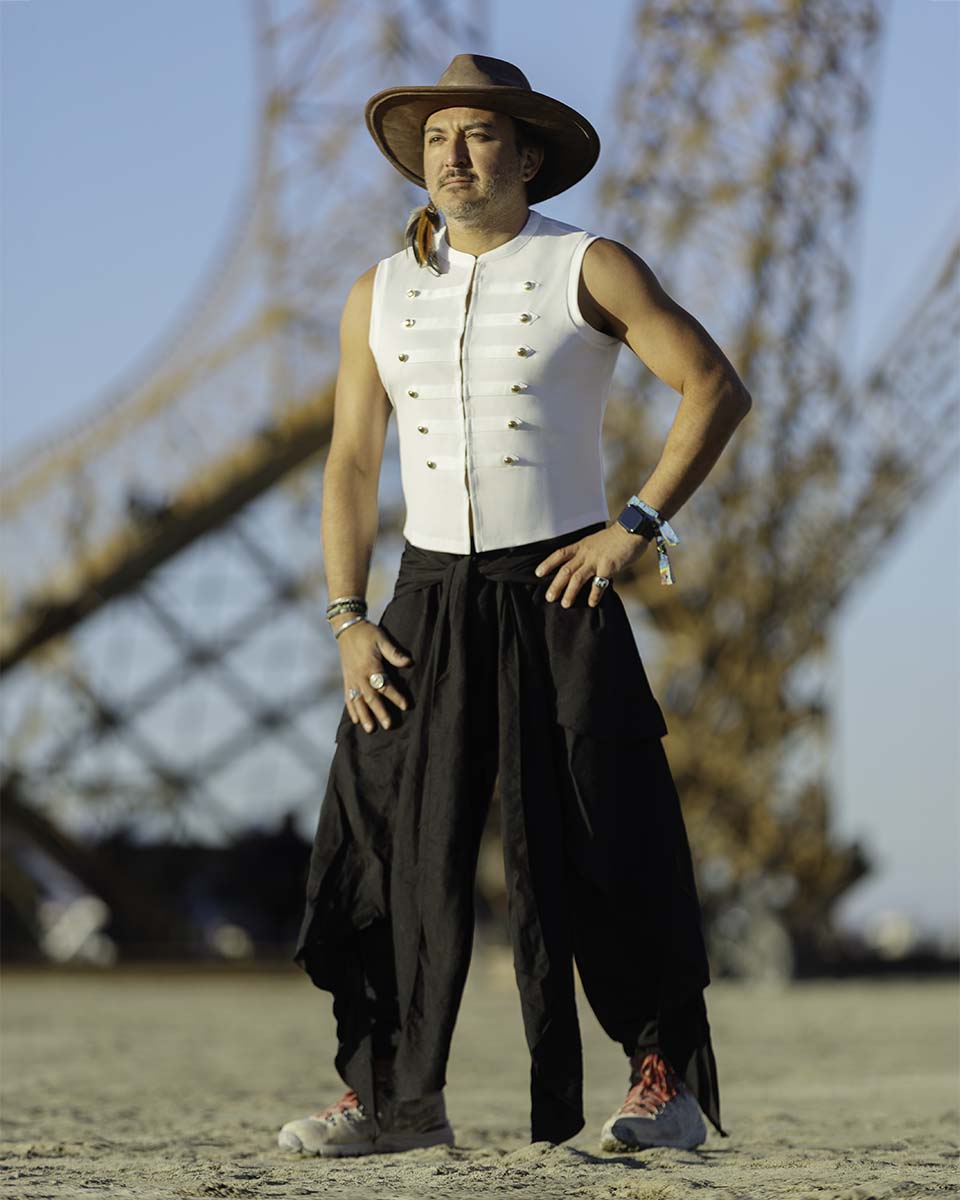 Phoenix Delgado in a hat and white vest in front of the Eiffel Tower art installation, Burning Man 2026, by Niaz Uddin