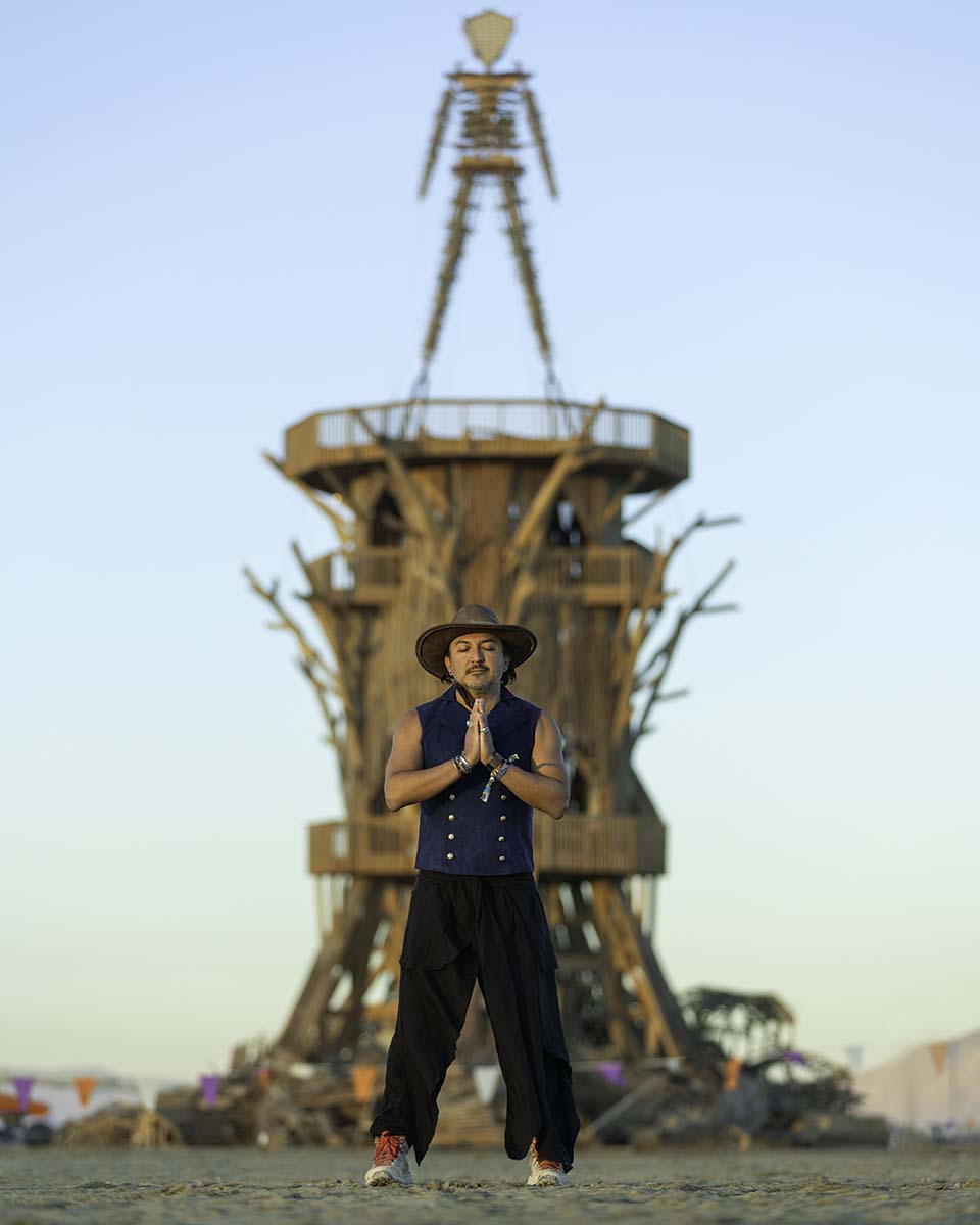 Phoenix Delgado with hands in prayer beneath the Man, Burning Man 2026, by Niaz Uddin