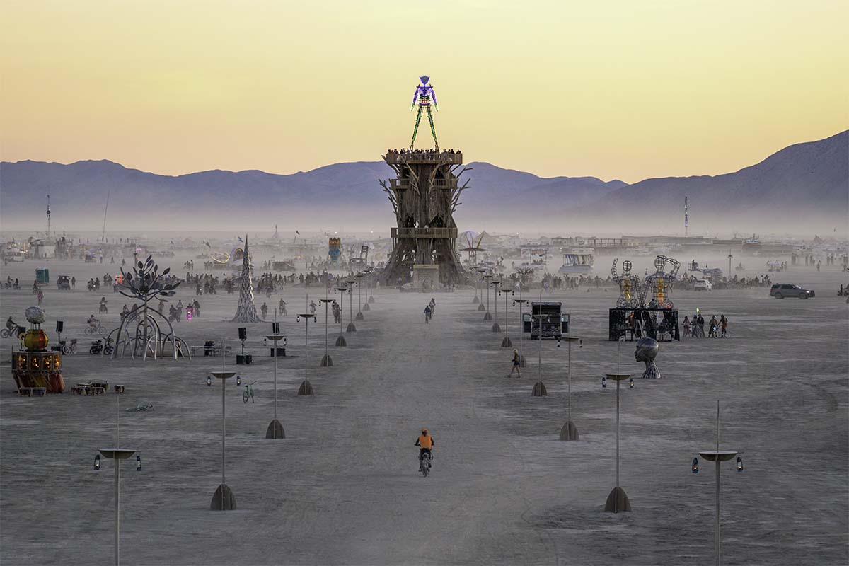 Cyclist on the lantern-lined path toward the Man at sunset, Burning Man 2026, by Niaz Uddin