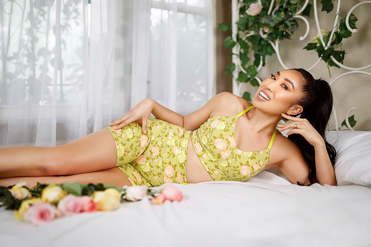Cassey Ho reclining on a white bed in the POPFLEX Rose Garden floral set surrounded by roses, by Niaz Uddin