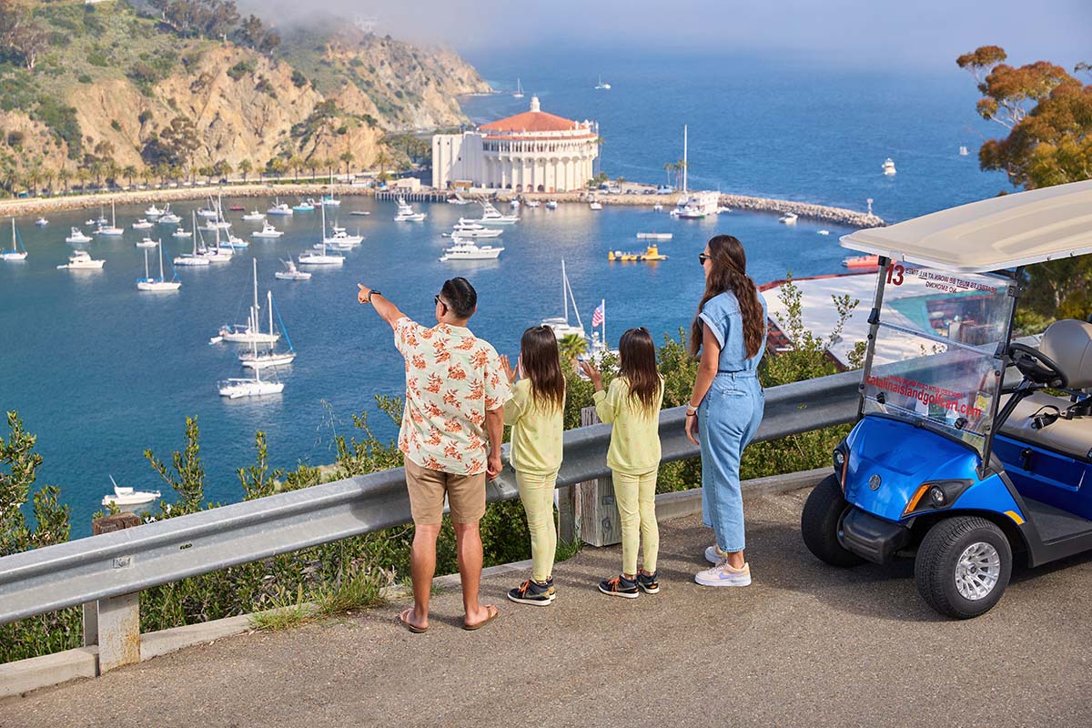 Family of four looking out at Avalon harbor and the Catalina Casino beside their golf cart, by Niaz Uddin