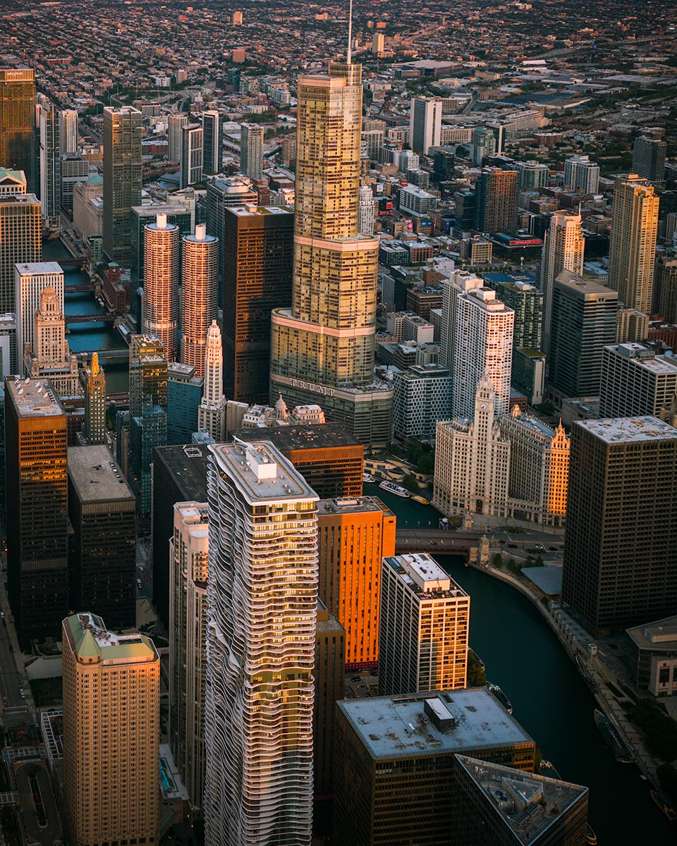 Vertical aerial view of Chicago with the Aqua Tower's rippling balconies in the foreground and Trump Tower rising behind, golden light on the Chicago River, by Niaz Uddin