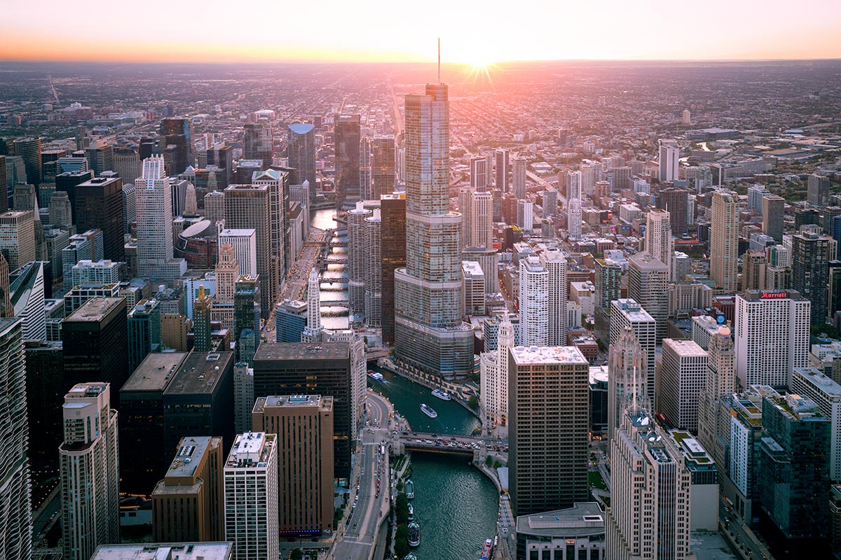 The sun setting directly behind the Trump Tower spire in an aerial view of Chicago, with the Chicago River and Wrigley Building below, by Niaz Uddin