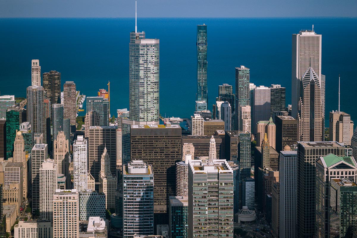 Aerial view of the Chicago skyline against the deep blue of Lake Michigan in daylight, with Trump Tower, the St. Regis Chicago, and the Aon Center, by Niaz Uddin