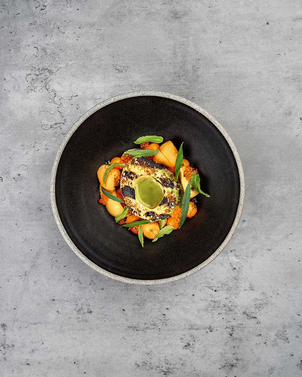 Fine dining plated dish with a charred center, green herb sauce, melon, salmon roe, and mint in a black ceramic bowl, by Niaz Uddin