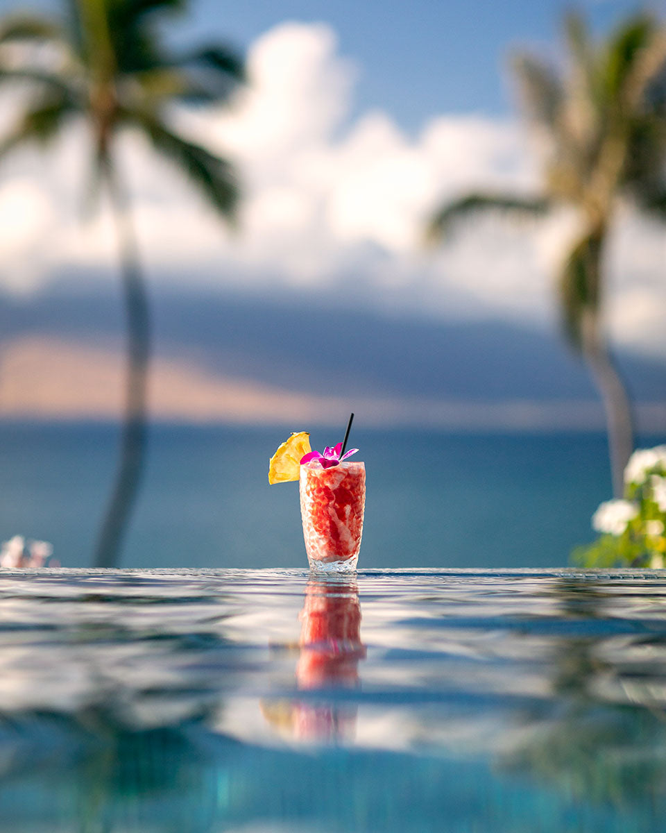 Tropical cocktail balanced on the infinity-pool edge with its reflection, ocean and palms behind, Four Seasons Resort Maui, by Niaz Uddin