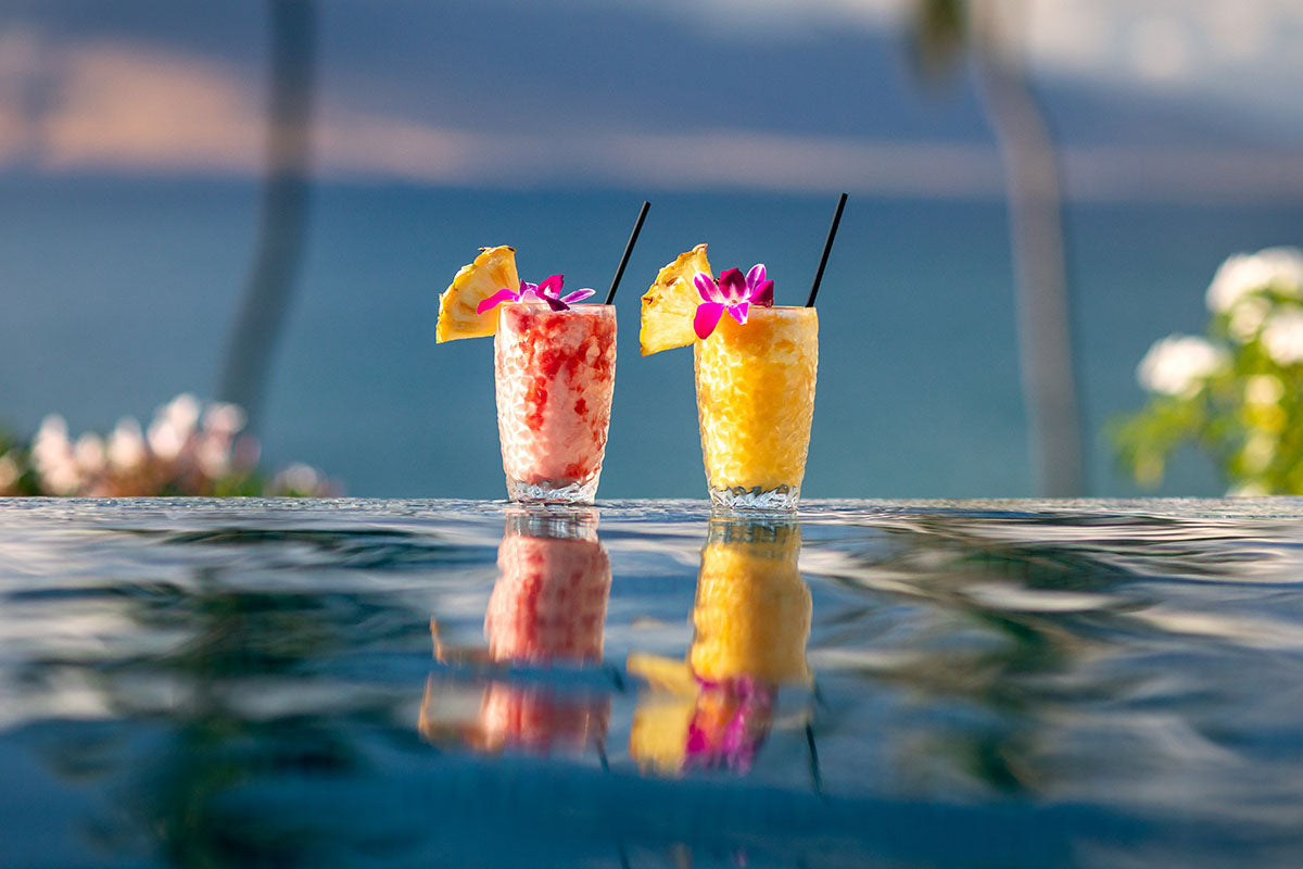 Pair of tropical cocktails on the infinity-pool edge with the ocean and palms behind, Four Seasons Resort Maui, by Niaz Uddin
