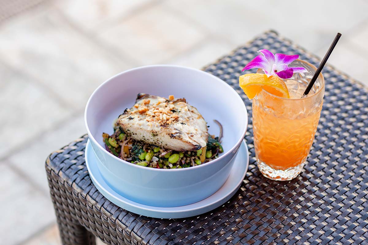 Grilled fish over a grain salad beside a tropical cocktail on a poolside table, Four Seasons Resort Maui, by Niaz Uddin