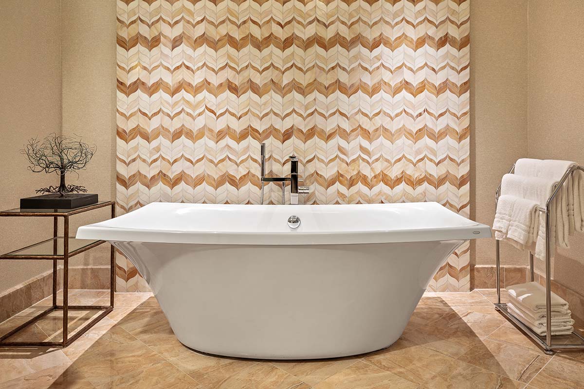 Freestanding soaking tub against an onyx chevron tile wall in a marble bath at Four Seasons Resort Maui, by Niaz Uddin