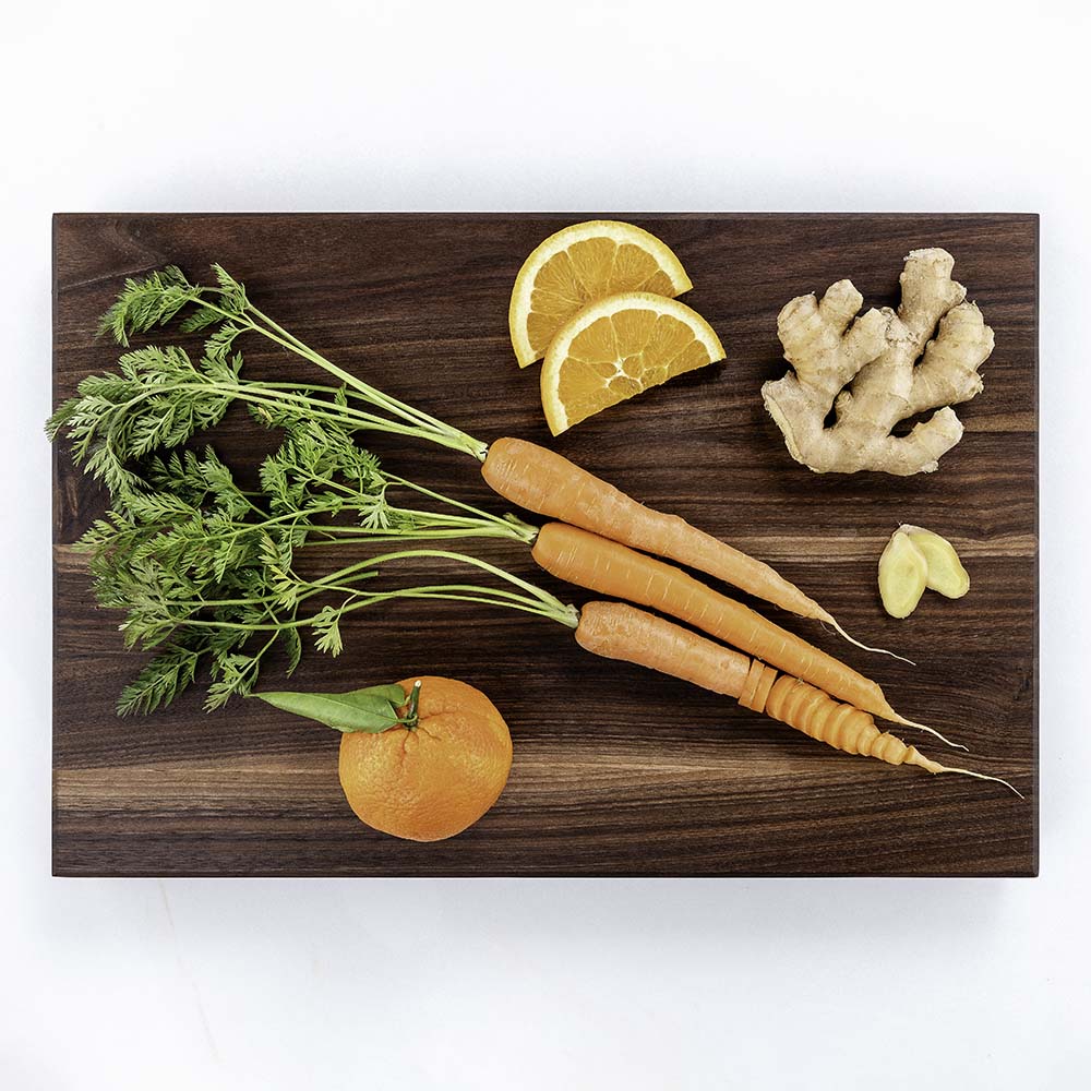 Carrots with their tops, ginger root, and an orange on a Hawker Woodcraft walnut cutting board, by Niaz Uddin