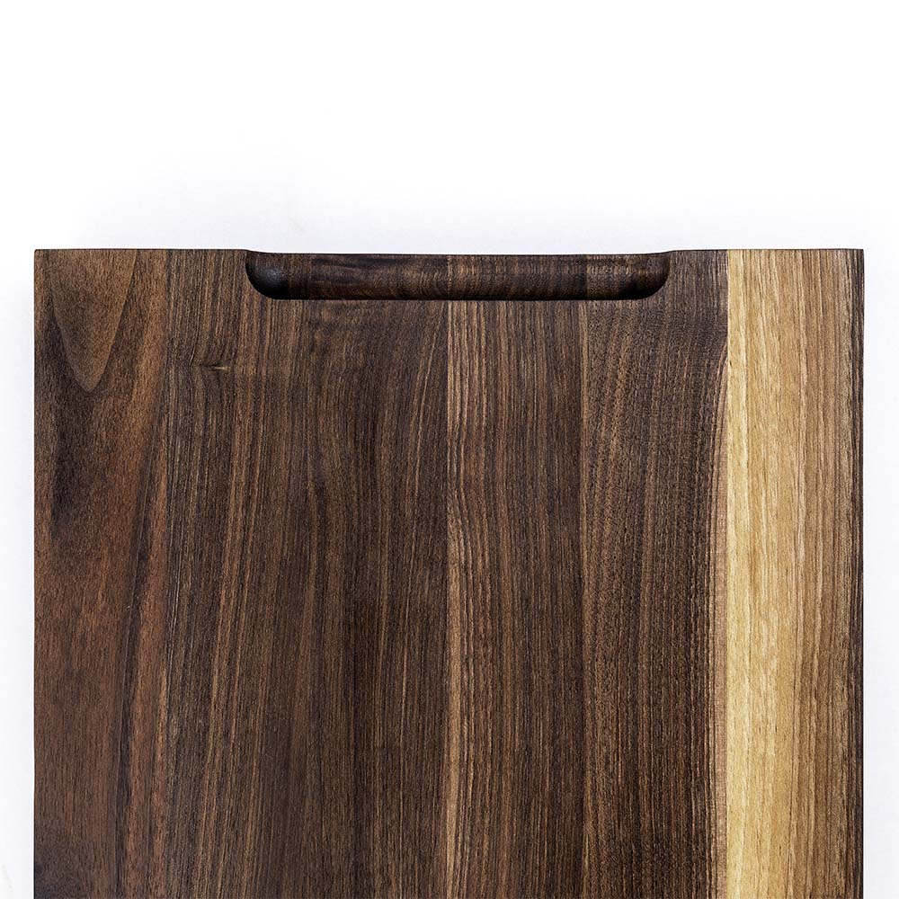 Top-down detail of a Hawker Woodcraft walnut cutting board with a carved handle notch and juice groove, by Niaz Uddin