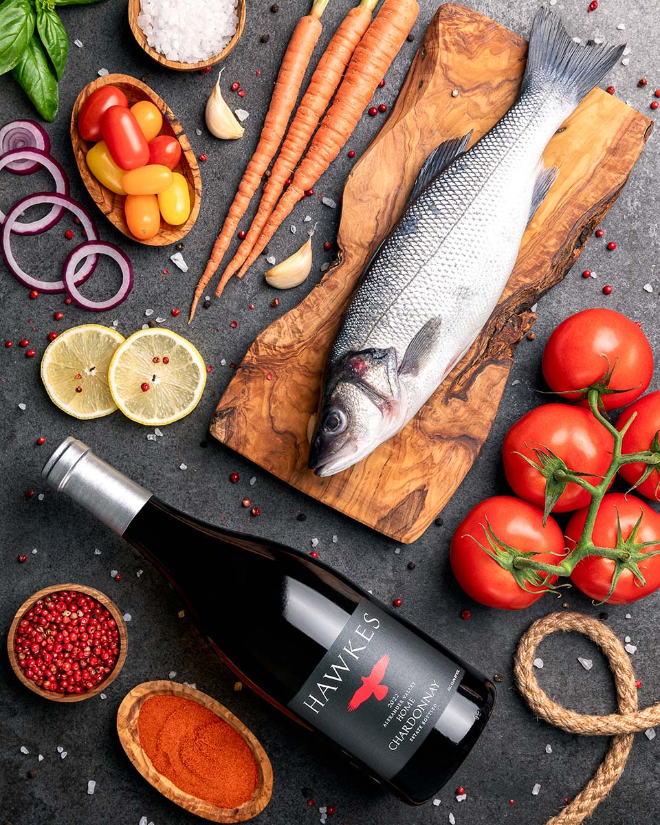 Hawkes Chardonnay with a whole raw sea bass on an olive-wood board, heirloom tomatoes, carrots, and spices, by Niaz Uddin
