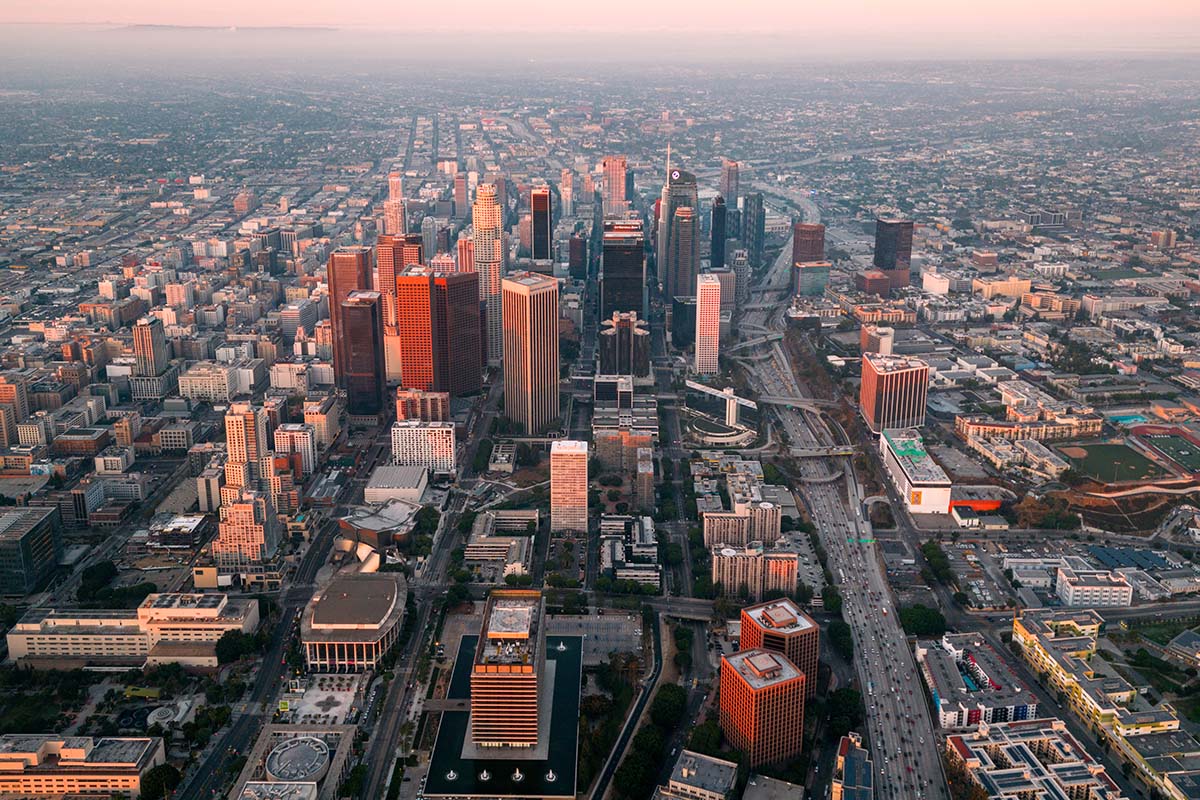 Aerial of a cluster of downtown Los Angeles towers lit by warm side light at golden hour, by Niaz Uddin