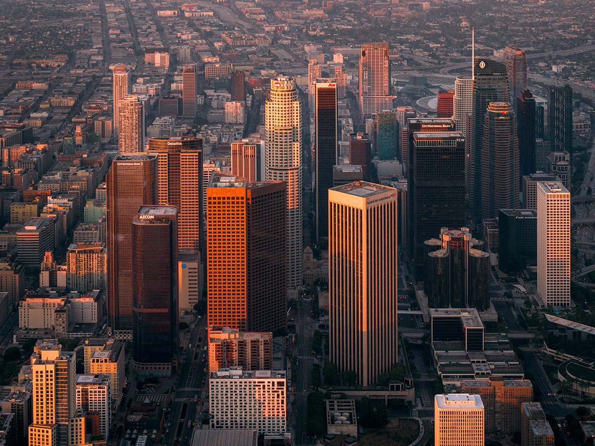 Aerial looking down a downtown Los Angeles avenue with warm golden light raking across the towers, by Niaz Uddin