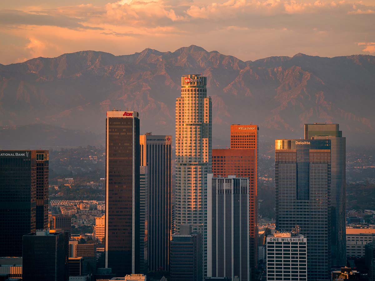 The US Bank Tower rising above the downtown Los Angeles skyline with the San Gabriel Mountains behind at golden hour, by Niaz Uddin
