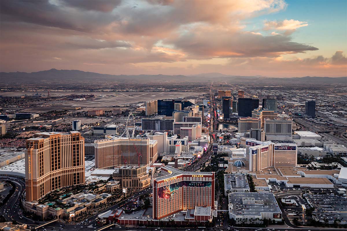 Sunset aerial of the Las Vegas Strip under pink clouds, looking south past the Palazzo, Venetian, and Treasure Island toward the mountains, by Niaz Uddin