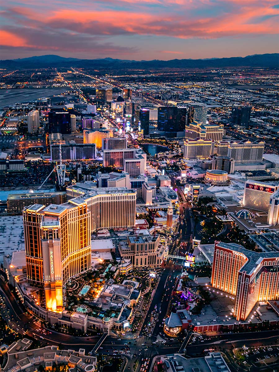 Vertical dusk aerial of the Las Vegas Strip with pink sunset clouds, the Palazzo and Venetian lit up as night falls, by Niaz Uddin