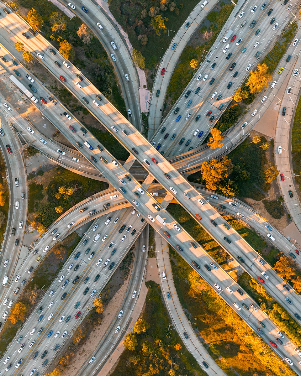 Aerial top-down view of a downtown Los Angeles freeway interchange with curving ramps and traffic at golden hour.