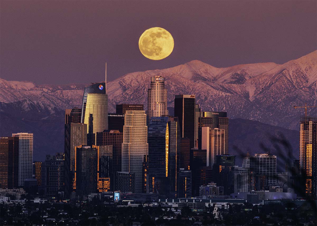 Full moon rising over the Los Angeles skyline and snowy mountains