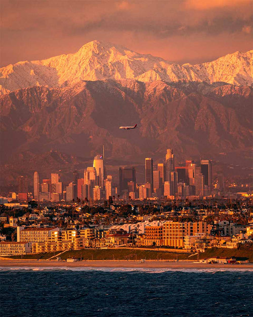 Snow-capped San Gabriel Mountains rising behind the downtown Los Angeles skyline and the Pacific Ocean at sunset, seen from Palos Verdes.