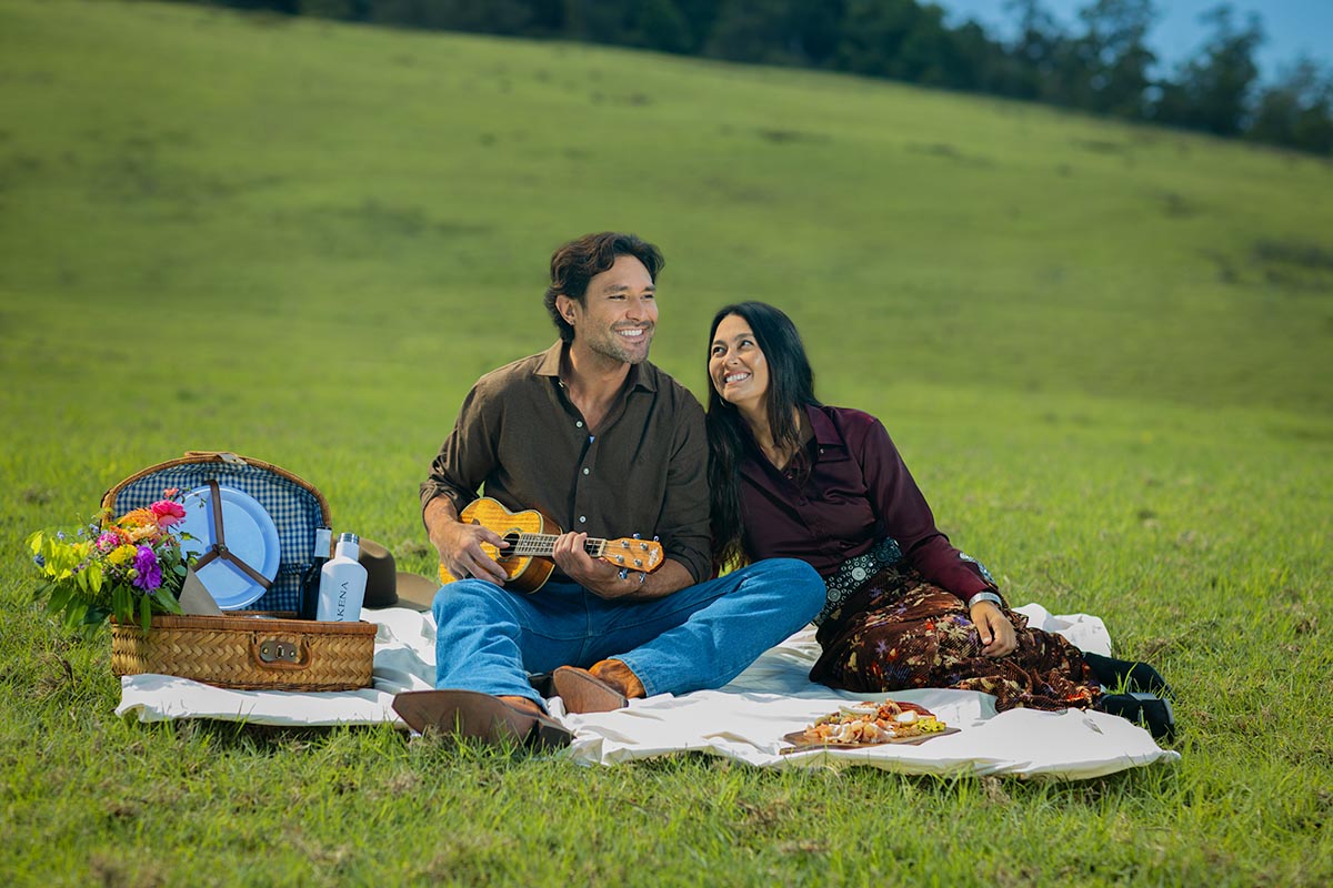 Couple leaning together as one plays ukulele on a hillside picnic blanket at Makena Beach Club, Maui, by Niaz Uddin
