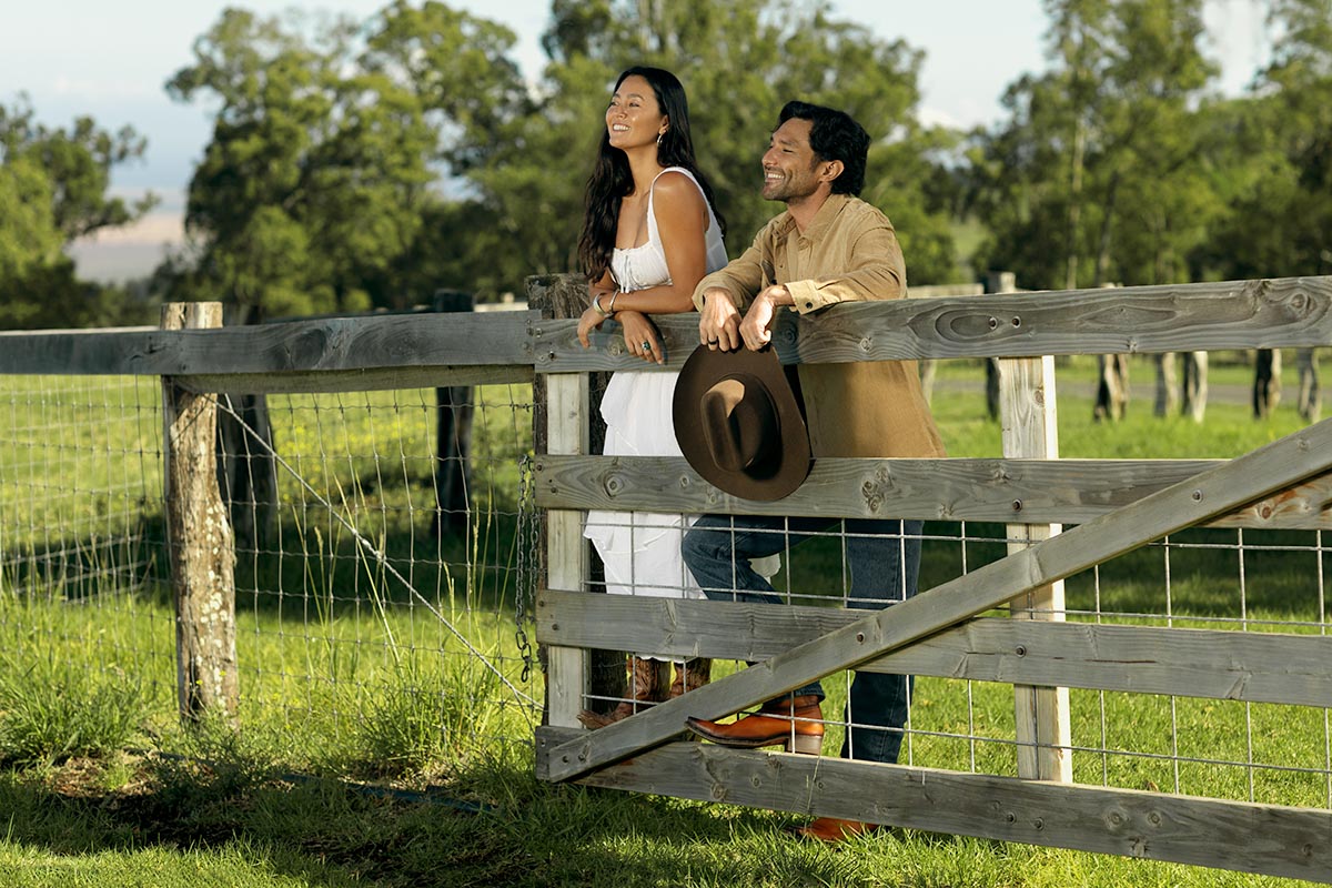 Couple at a ranch fence gazing out over the pasture and hills at Makena Beach Club, Maui, by Niaz Uddin