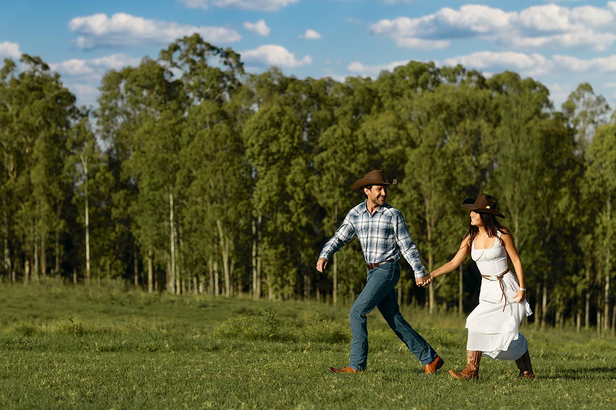Couple in cowboy hats walking hand in hand across an open pasture at Makena Beach Club, Maui, by Niaz Uddin