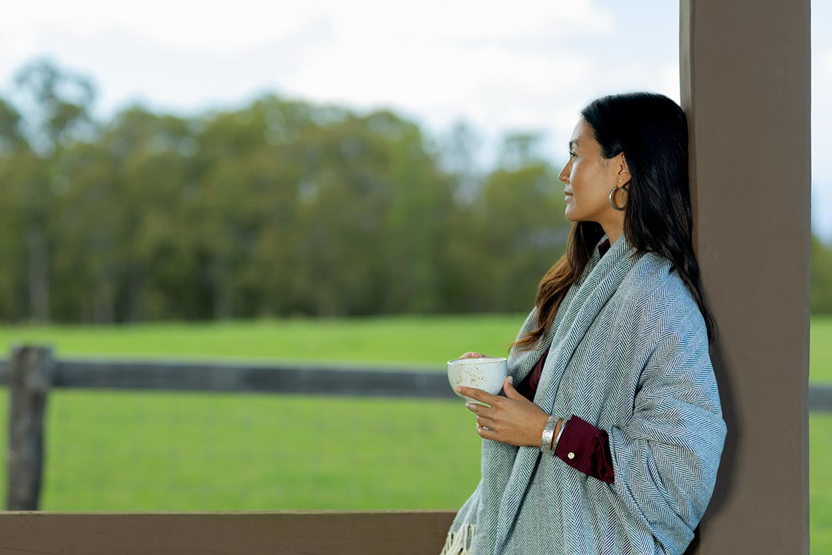 Woman wrapped in a throw blanket holding coffee with a pasture view at Makena Beach Club, Maui, by Niaz Uddin