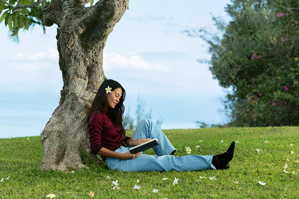 Woman with a plumeria in her hair reading under a tree at Makena Beach Club, Maui, by Niaz Uddin