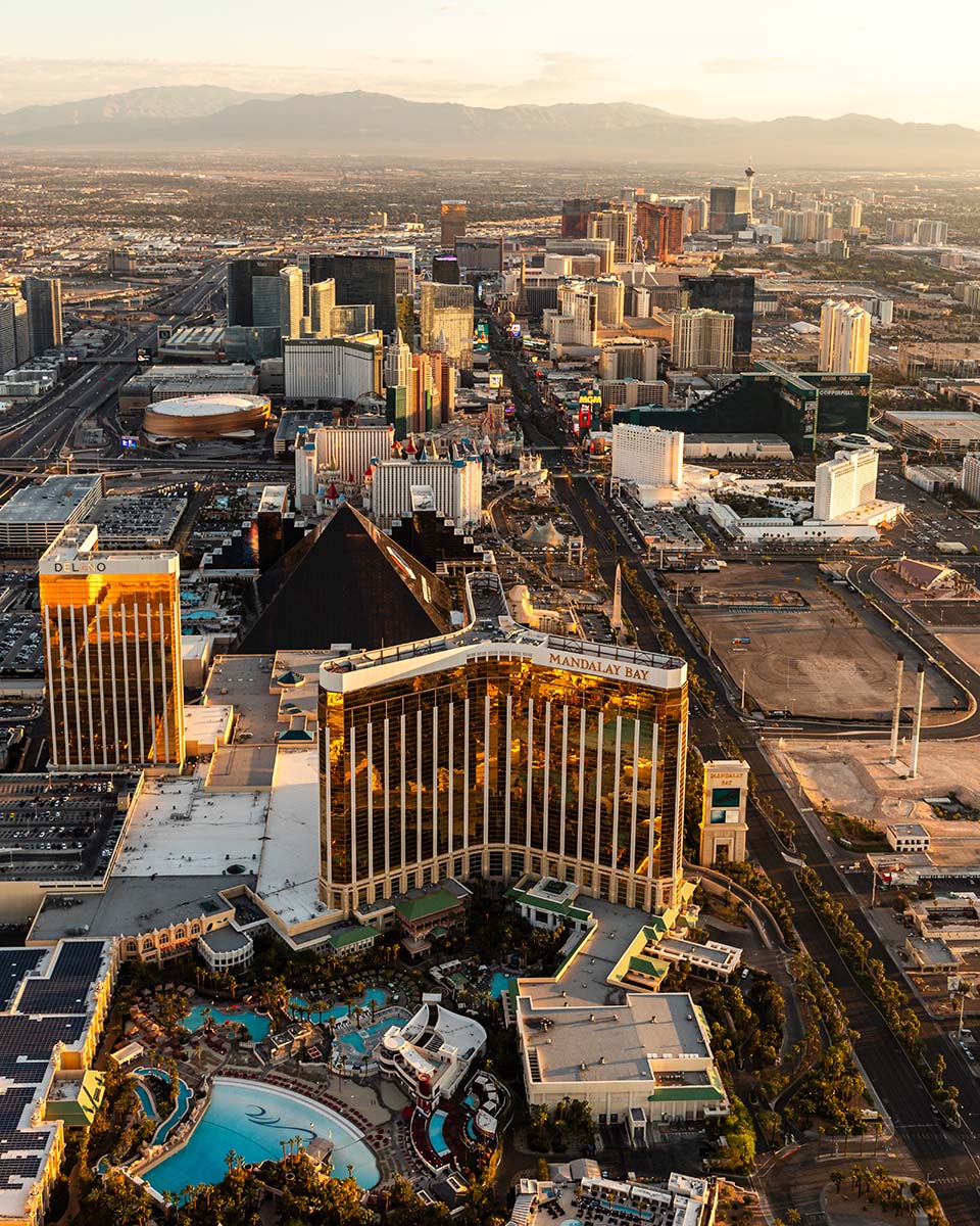 Vertical golden-hour aerial of the south Las Vegas Strip with Mandalay Bay, the Luxor pyramid, and the Delano, the skyline stretching to the mountains, by Niaz Uddin