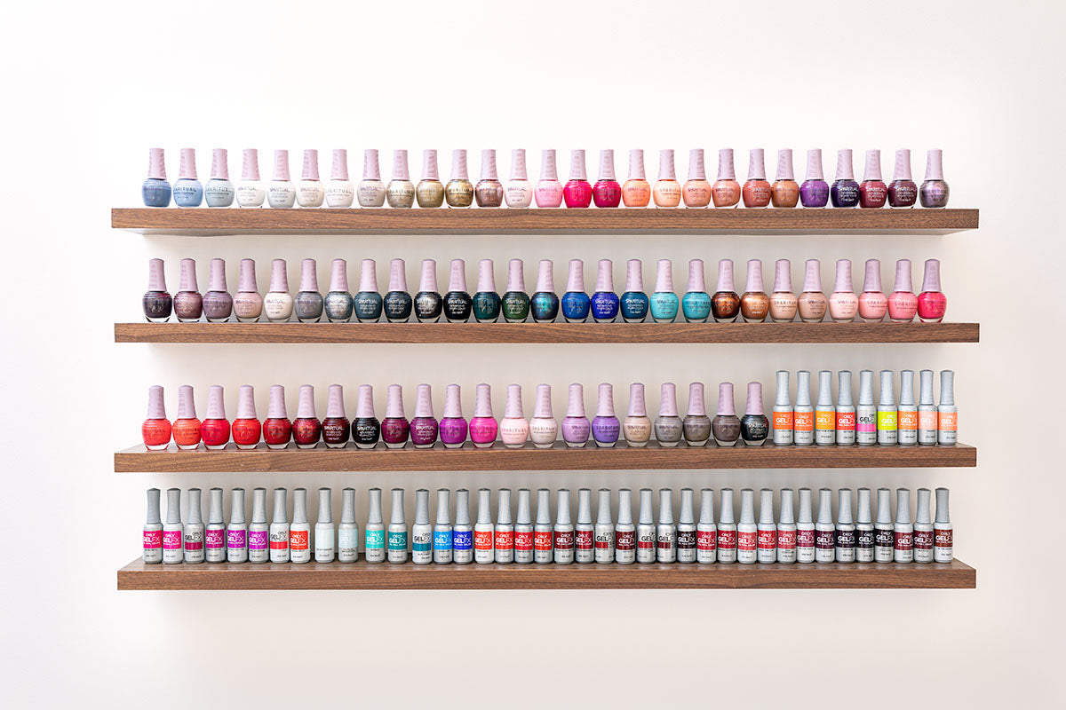 milk + honey nail bar wall with rows of polish bottles arranged across the color spectrum on walnut shelves, by Niaz Uddin