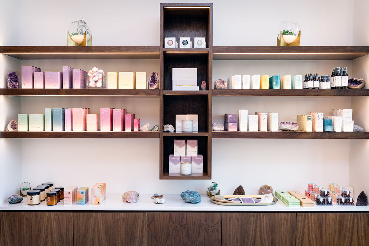 milk + honey retail wall with products arranged in a color gradient on walnut shelves accented by amethyst geodes, by Niaz Uddin