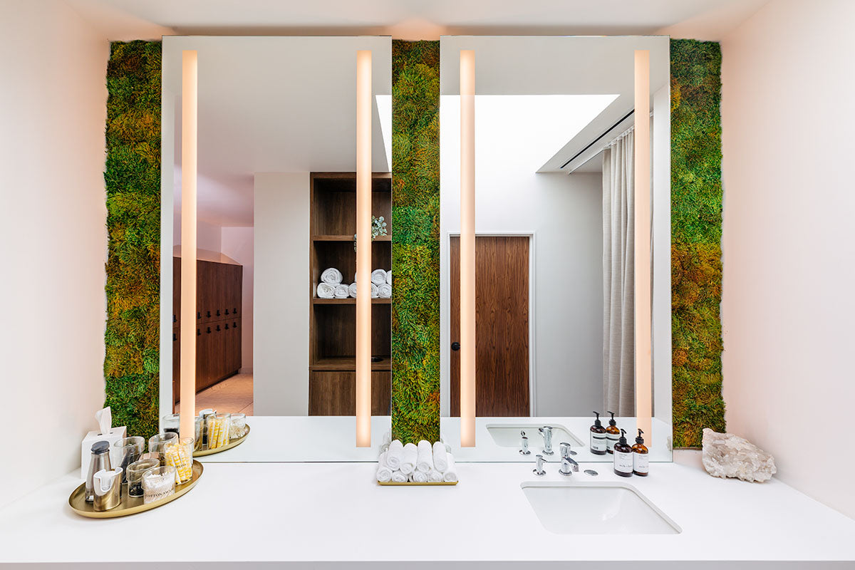 milk + honey vanity with twin lit mirrors framed by living moss walls, rolled towels, amenities, and a quartz cluster, by Niaz Uddin