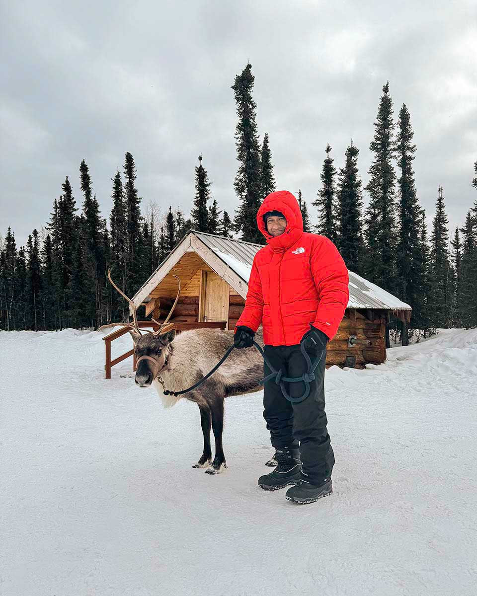Niaz Uddin in a red winter jacket with a reindeer in Alaska