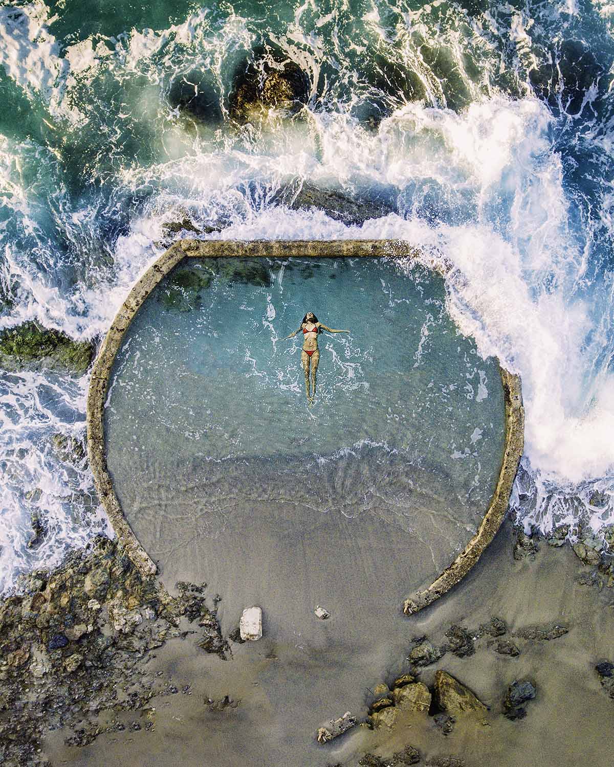 Top-down aerial of a lone swimmer in an ocean tide pool in California