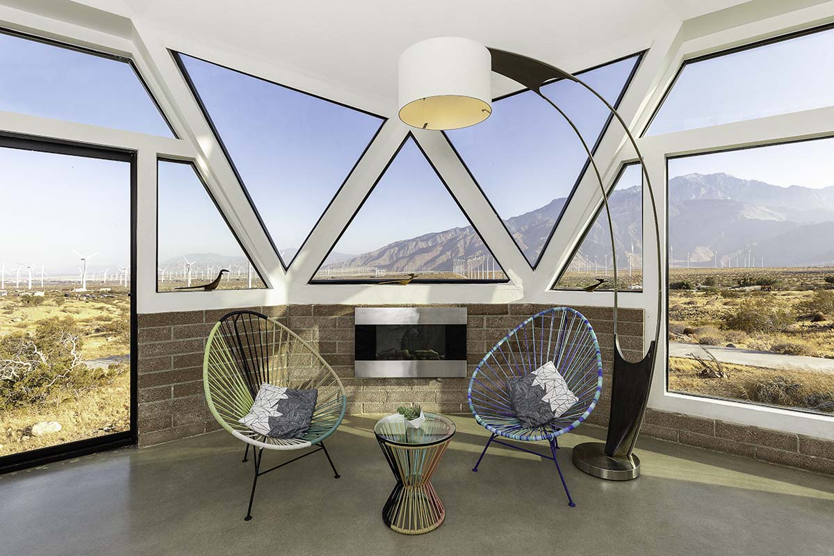 Interior dome lounge with triangular geometric windows, Acapulco chairs, and a mountain and wind-farm view, in the Palm Springs dome house, by Niaz Uddin