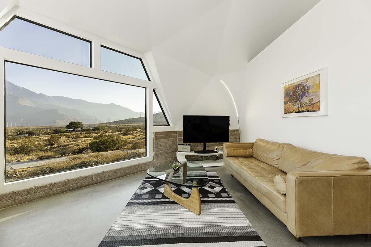 Living room with a leather sofa and angled window framing the desert and mountains in the Palm Springs dome house, by Niaz Uddin