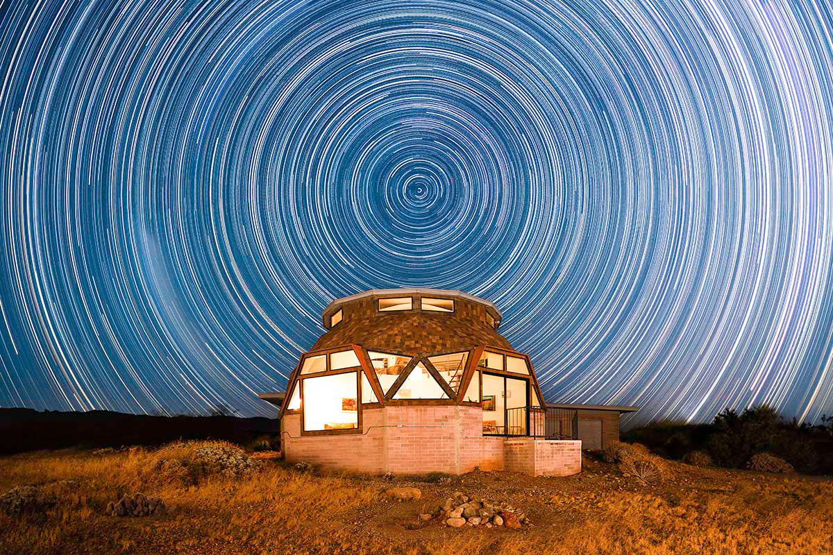 Long-exposure star trails circling the celestial pole above the glowing geodesic dome house at night in the Palm Springs desert, by Niaz Uddin