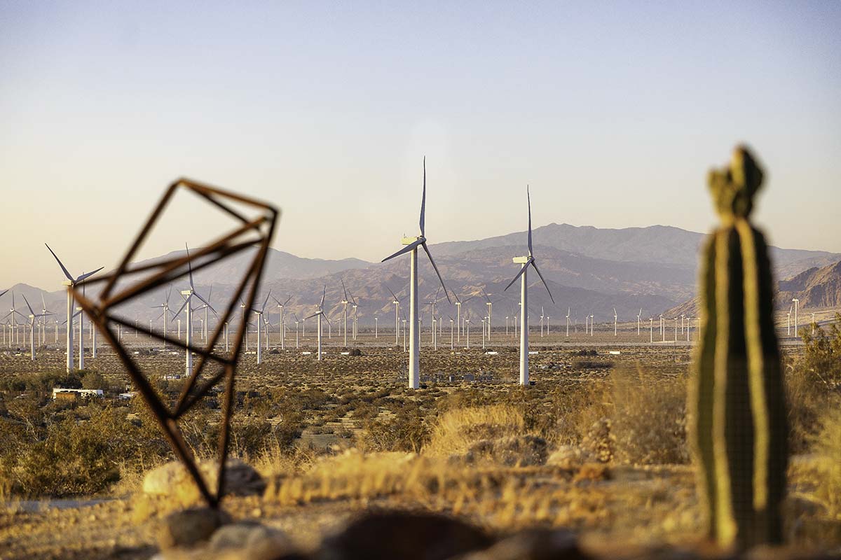 Wind turbines across the desert with a geometric metal sculpture and cactus in the foreground, near Palm Springs, by Niaz Uddin