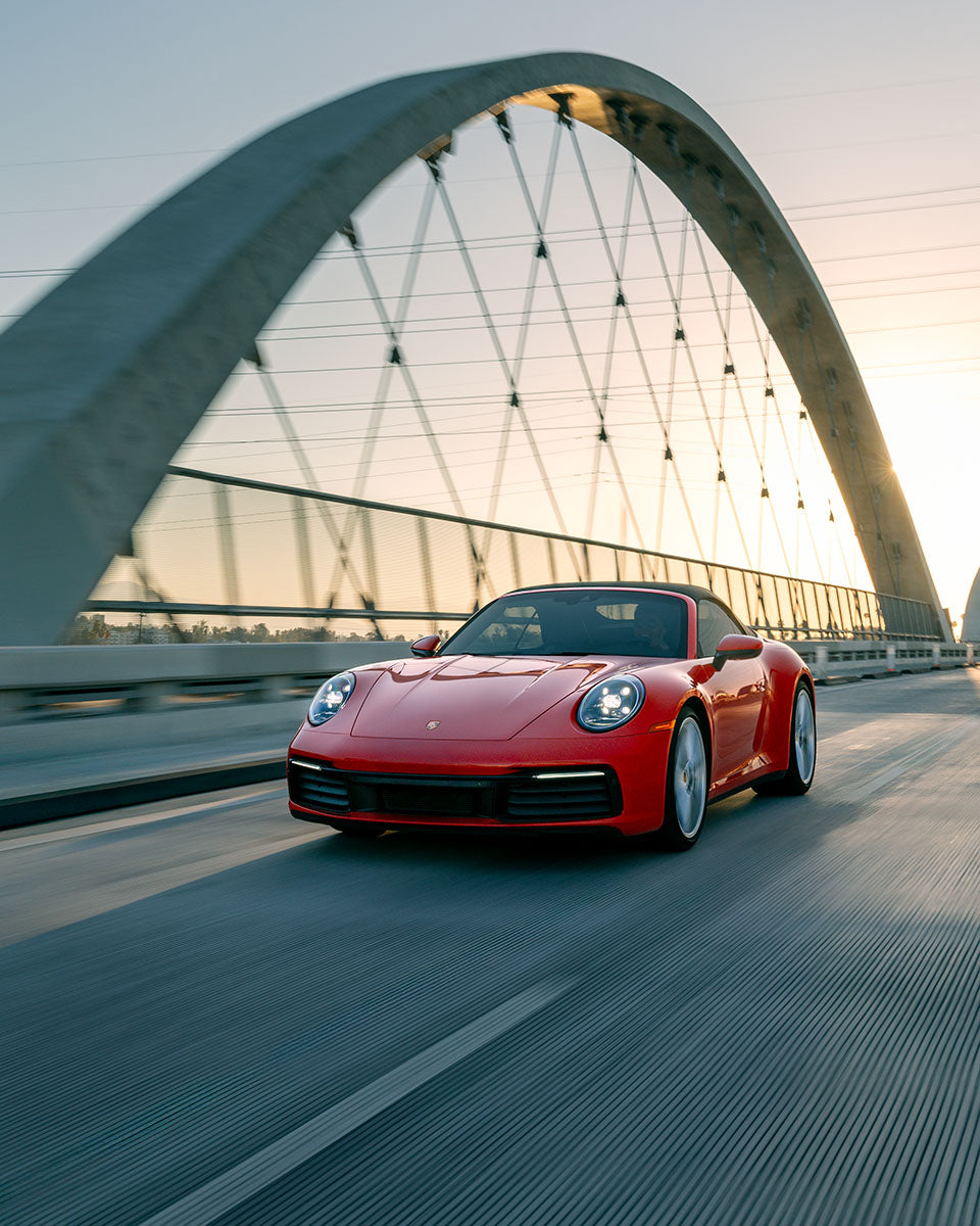 Red Porsche 911 Carrera cabriolet driving toward camera across the 6th Street Bridge with the downtown Los Angeles skyline behind, by Niaz Uddin
